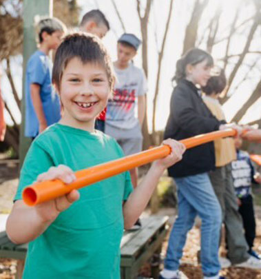 A boy holds an orange pole, surrounded by children at Camp Fairbridge's School Camp