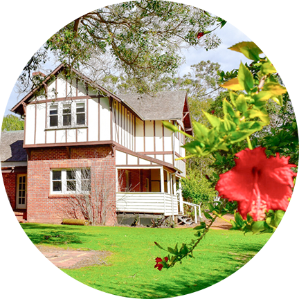 A charming house surrounded by a garden with tall trees, located in the southwest accommodation area