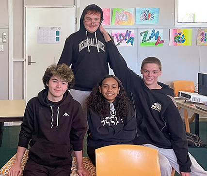 Four people in black hoodies, having photoshoot in Fairbridge's School Camp classroom