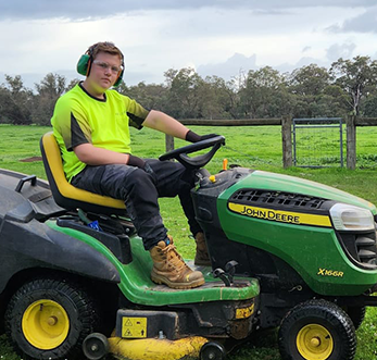 Jarvis, a trainee at Fairbridge, seated on a green lawn mower, enjoying a sunny day at a school camp in Pinjarra Fairbridge